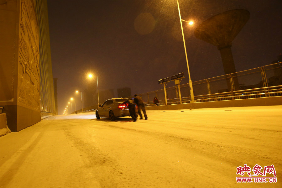 雪天路滑，汽車上橋打滑，兩名“推車人”幫助一輛私家車上坡。